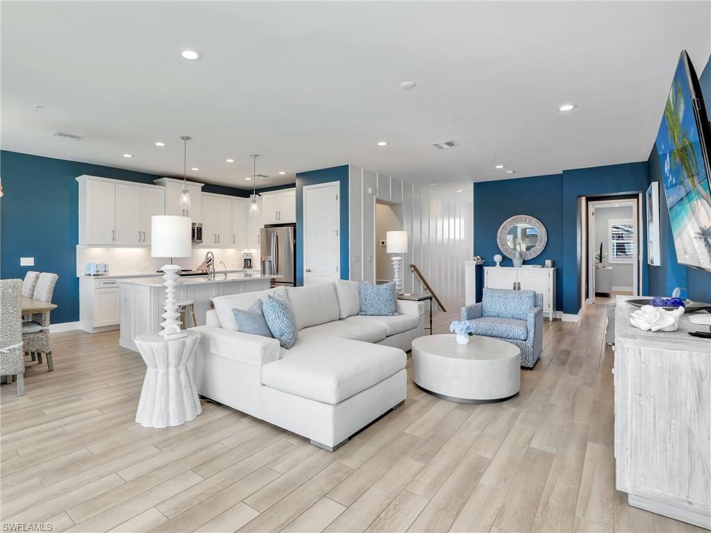 a living room with white couches and kitchen view with wooden floor