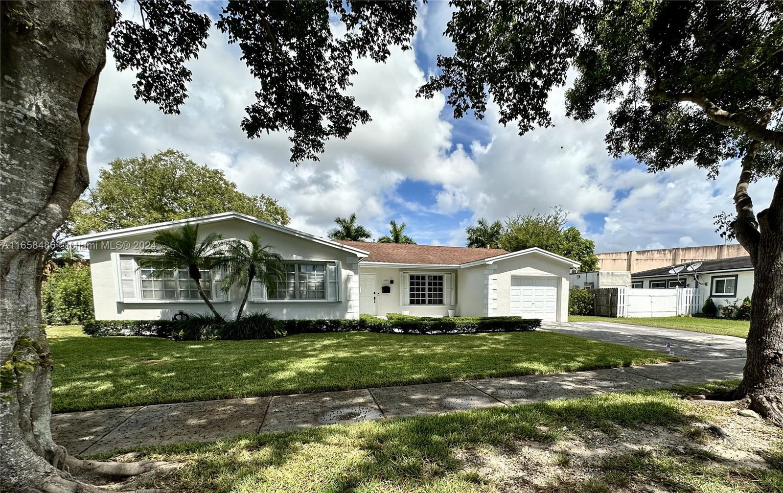 a view of a white house next to a yard with big trees