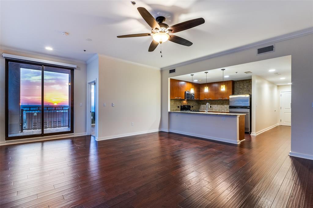 a view of an empty room with wooden floor and a kitchen