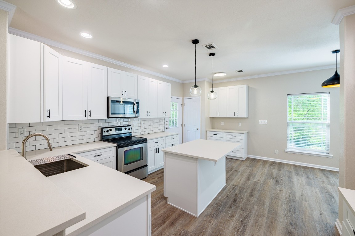 a kitchen with a stove a sink a refrigerator and white cabinets with wooden floor