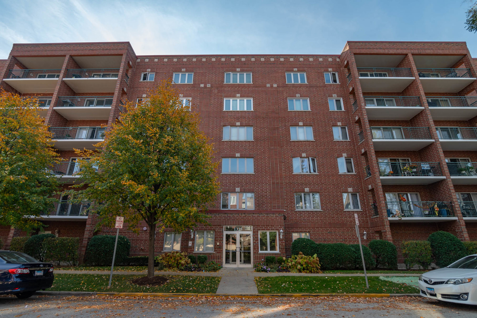 a front view of a building with lot of trees and plants