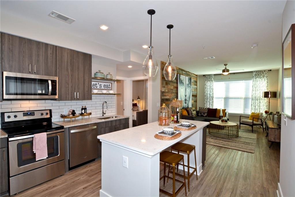 a kitchen with stainless steel appliances kitchen island granite countertop a stove a sink a microwave a dining table and chairs with wooden floor