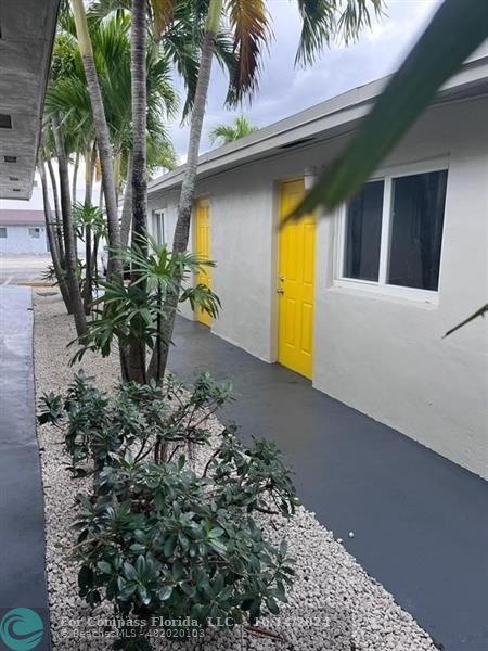 a view of yellow house with large trees and plants