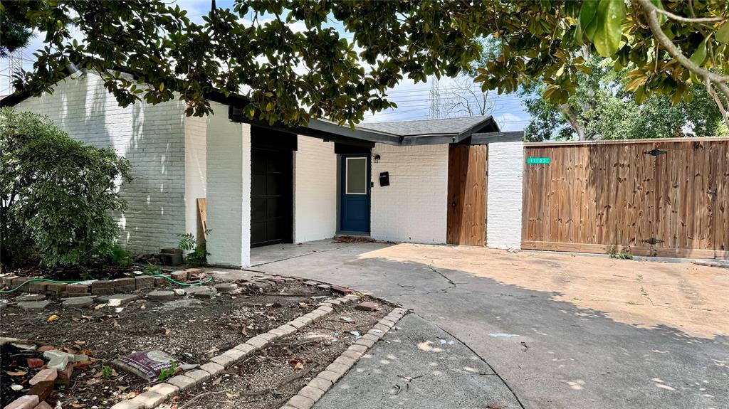 Charming white brick home with a cozy driveway, a private wooden fence, and serene tree canopy views.