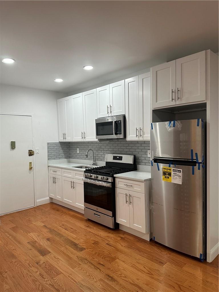 Kitchen featuring light hardwood / wood-style floors, tasteful backsplash, white cabinetry, and stainless steel appliances