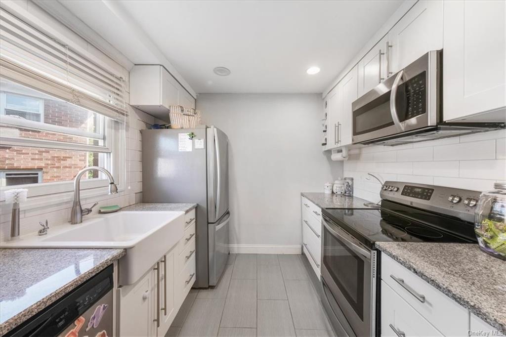 Kitchen featuring stainless steel appliances, white cabinets, light stone countertops, and backsplash