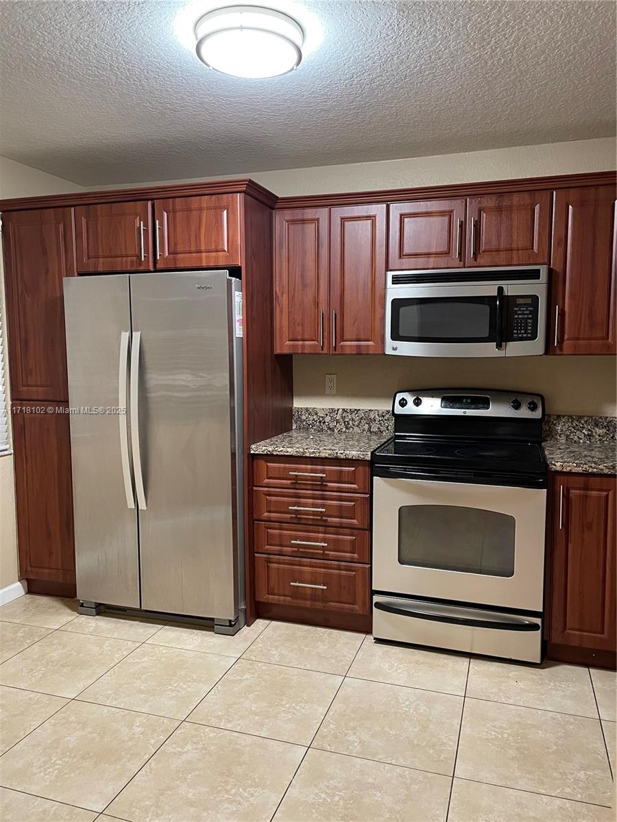 a kitchen with granite countertop a refrigerator and a stove top oven