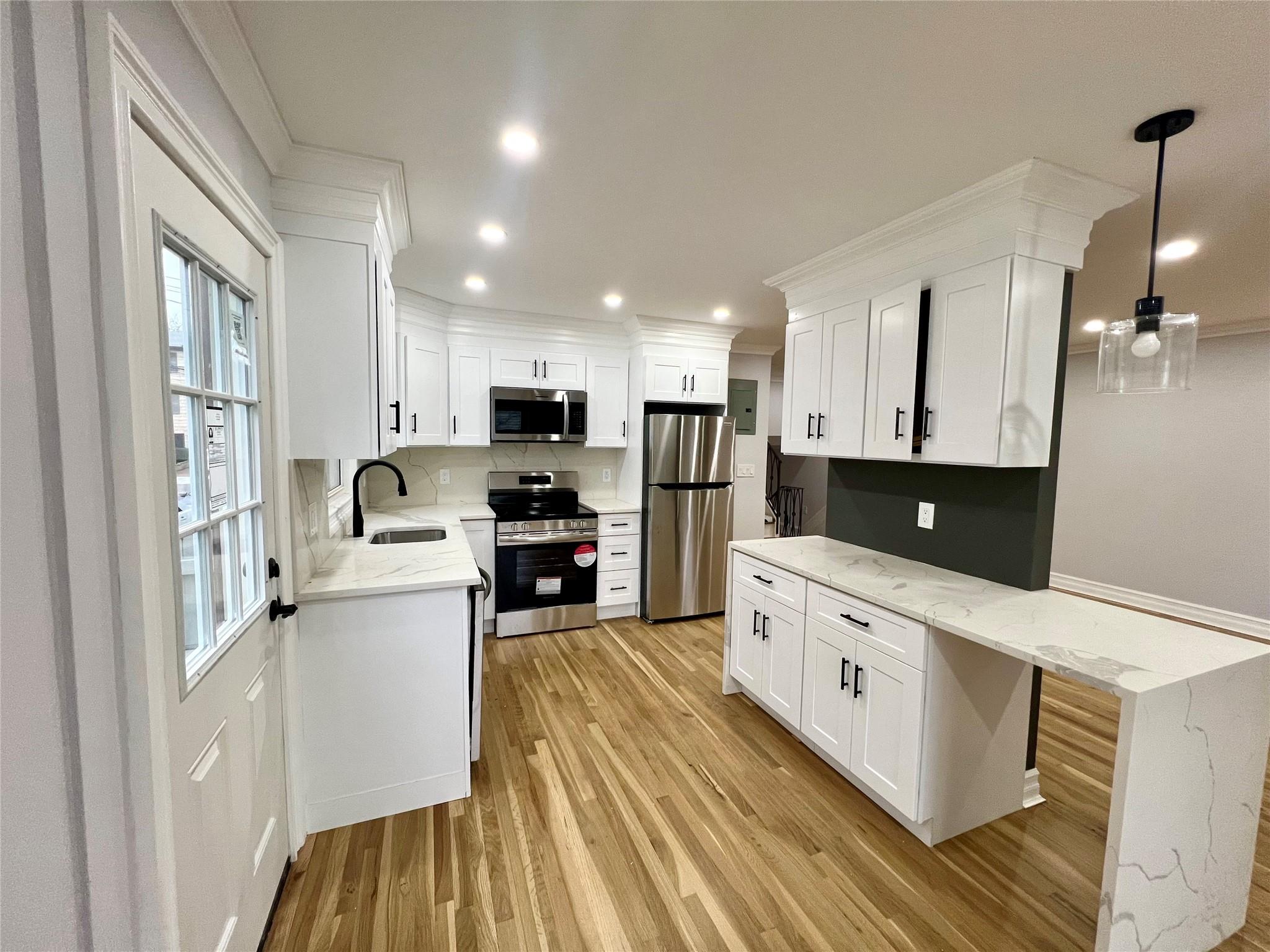 Kitchen with white cabinets, hanging light fixtures, light hardwood / wood-style flooring, light stone counters, and stainless steel appliances