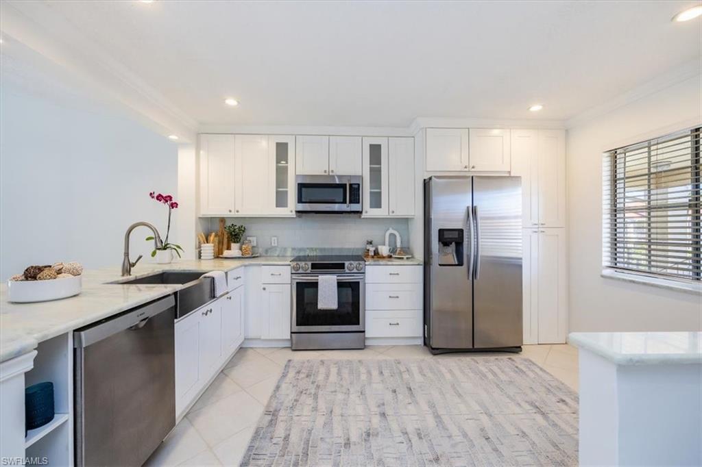 Kitchen with white cabinetry, stainless steel appliances, crown molding, and light tile flooring