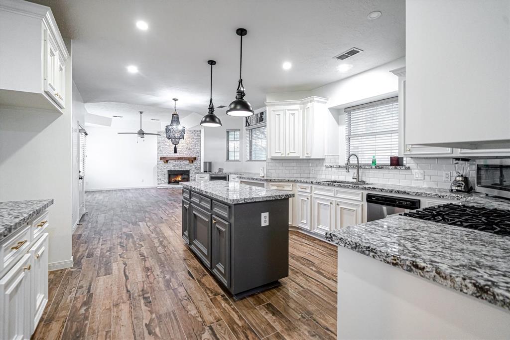 a large kitchen with stainless steel appliances granite countertop a stove a sink dishwasher a microwave oven and a large island with wooden floor