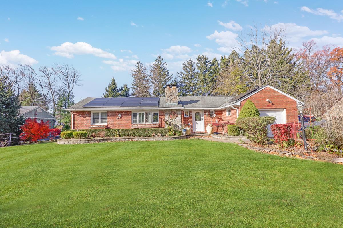 Ranch-style home with solar panels, a garage, and a front lawn