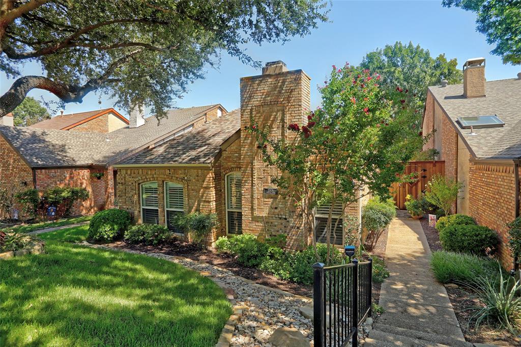 a view of a house with brick walls plants and large tree