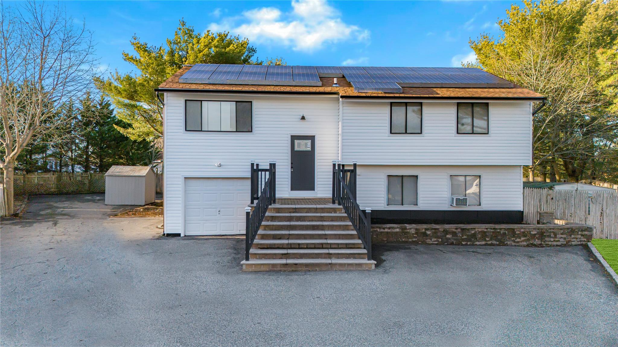 Bi-level home featuring cooling unit, a storage unit, solar panels, and a garage