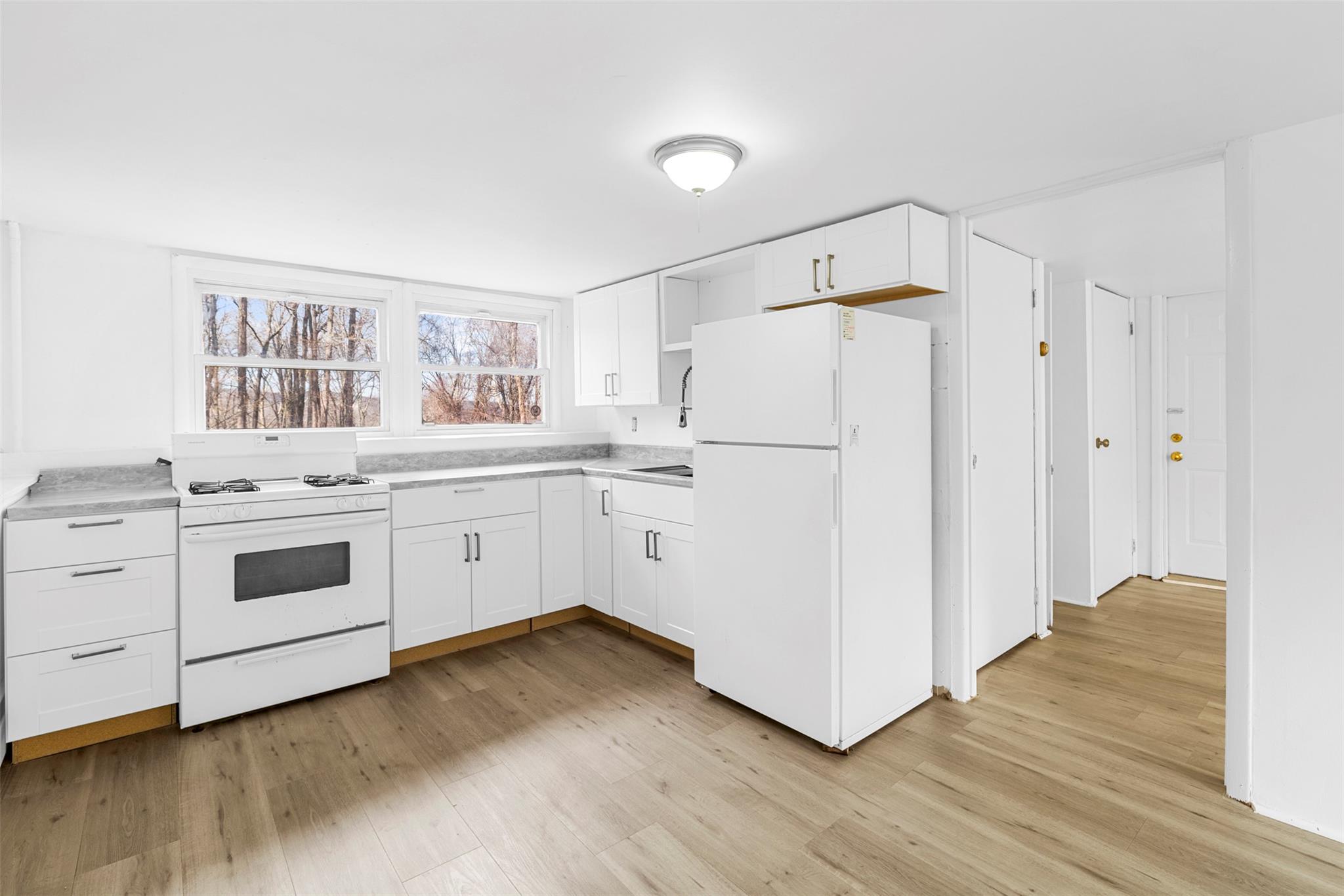 Kitchen with white cabinets, white appliances, and light hardwood / wood-style flooring