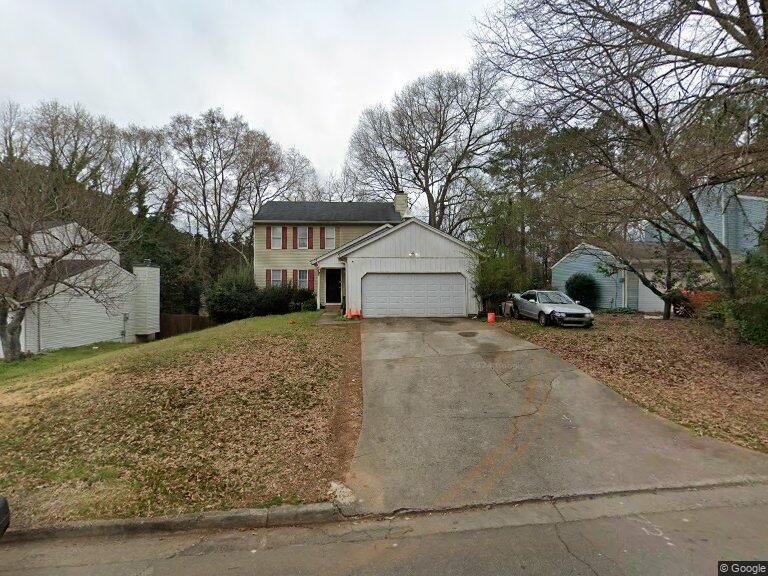 a view of a white house next to a yard with a large tree