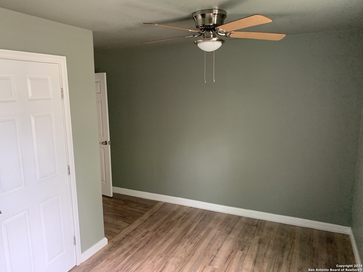 an empty room with wooden floor fan and windows