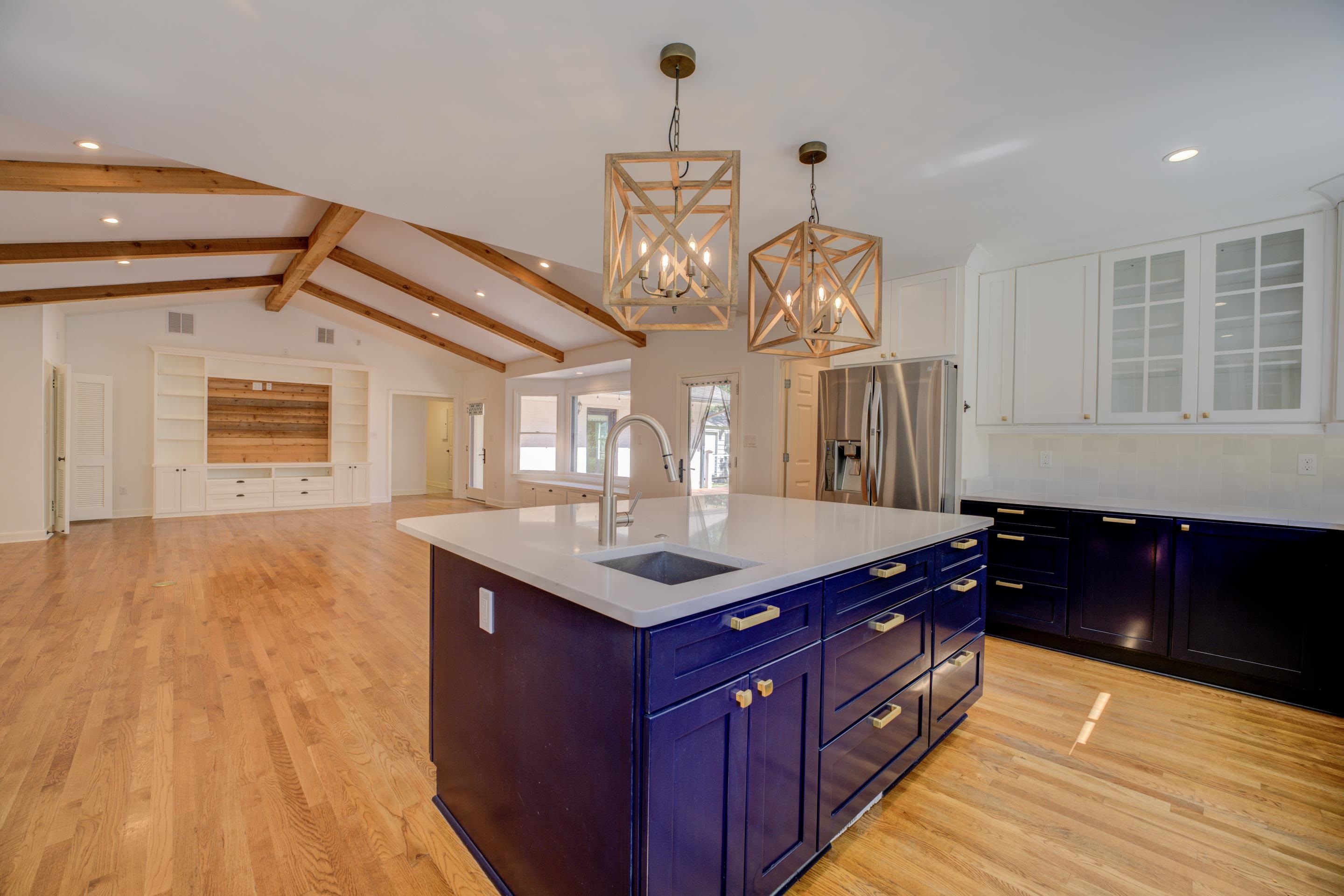 Kitchen featuring sink, hanging light fixtures, stainless steel refrigerator with ice dispenser, vaulted ceiling with beams, and white cabinetry