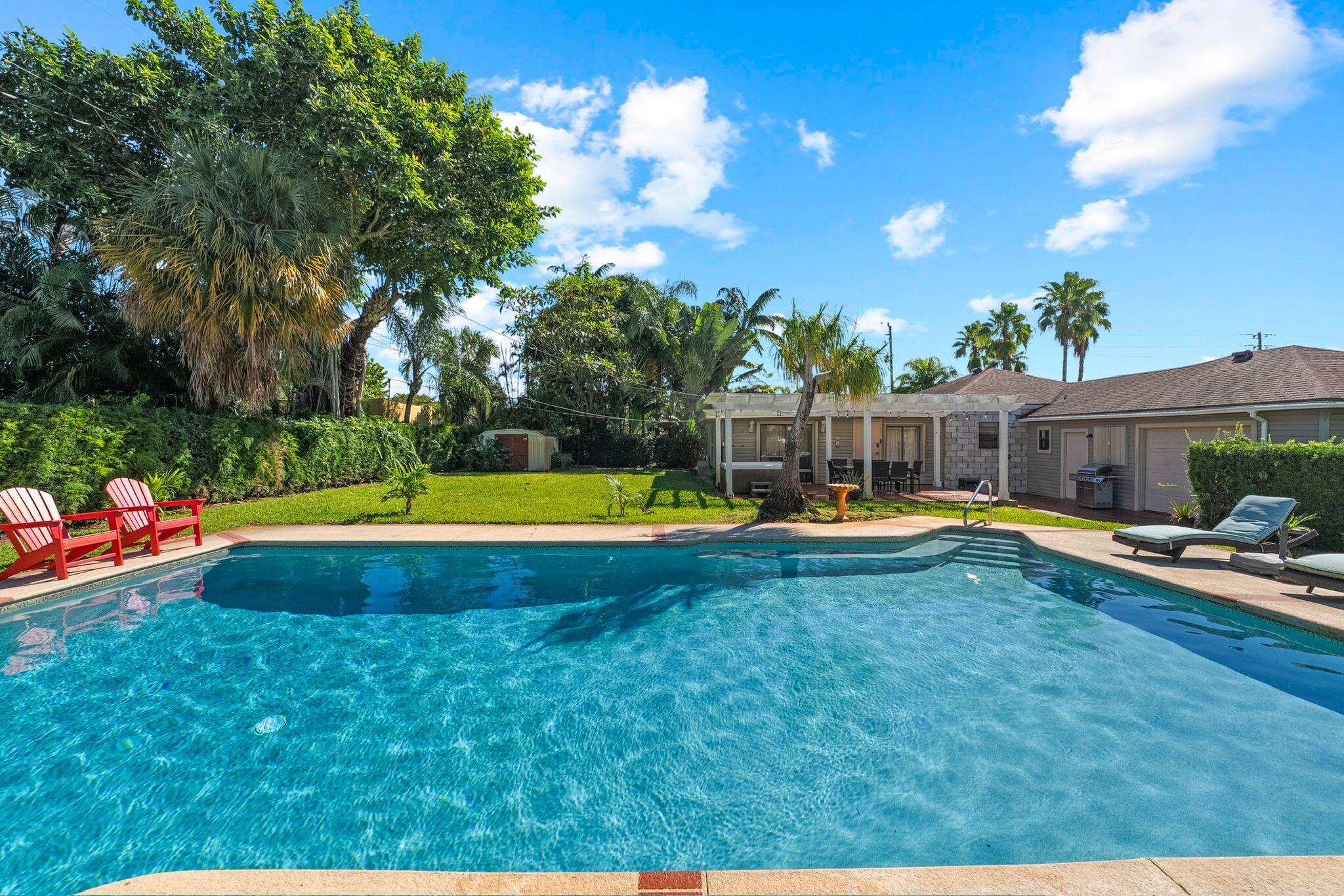 a view of swimming pool with lawn chairs and large trees