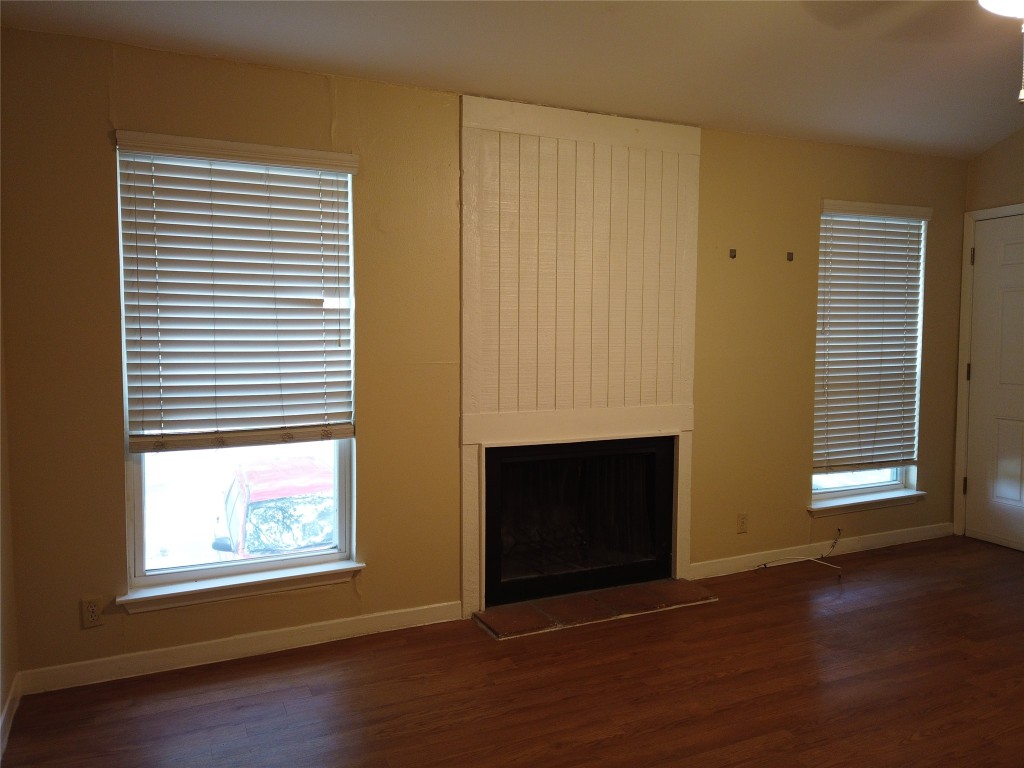 an empty room with wooden floor fireplace and windows