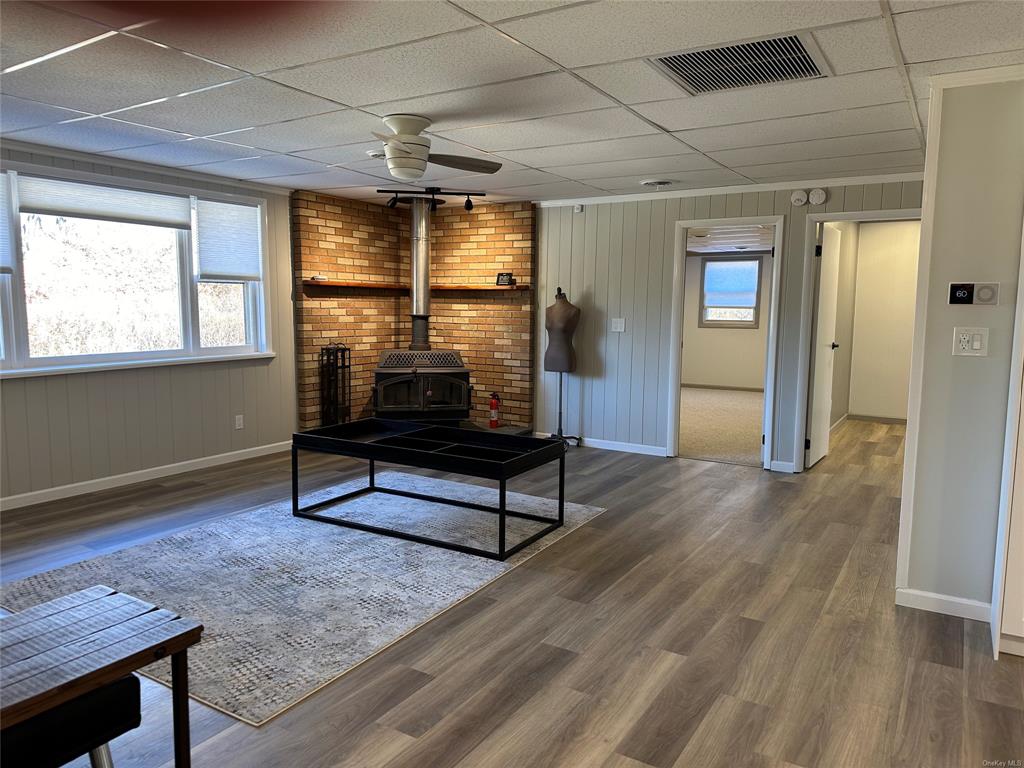 Living room featuring a paneled ceiling, dark hardwood / wood-style floors, ceiling fan, and a wood stove