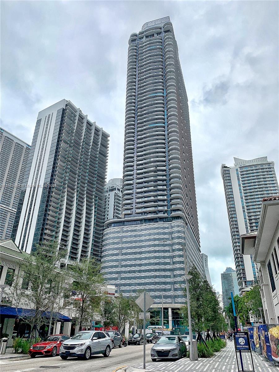 a front view of a building with lot of cars and trees