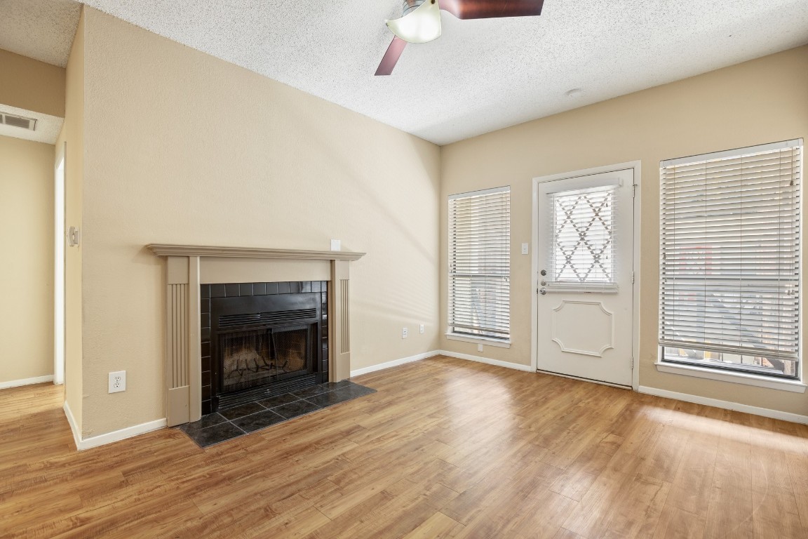 a view of an empty room with wooden floor fireplace and a window