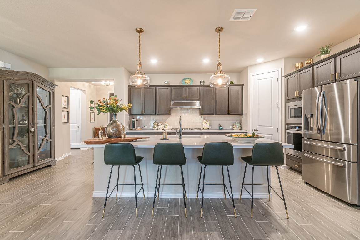 a kitchen with stainless steel appliances granite countertop a dining table chairs refrigerator and wooden floor