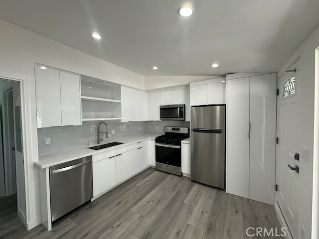 a kitchen with stainless steel appliances a refrigerator a sink dishwasher a stove and white cabinets with wooden floor