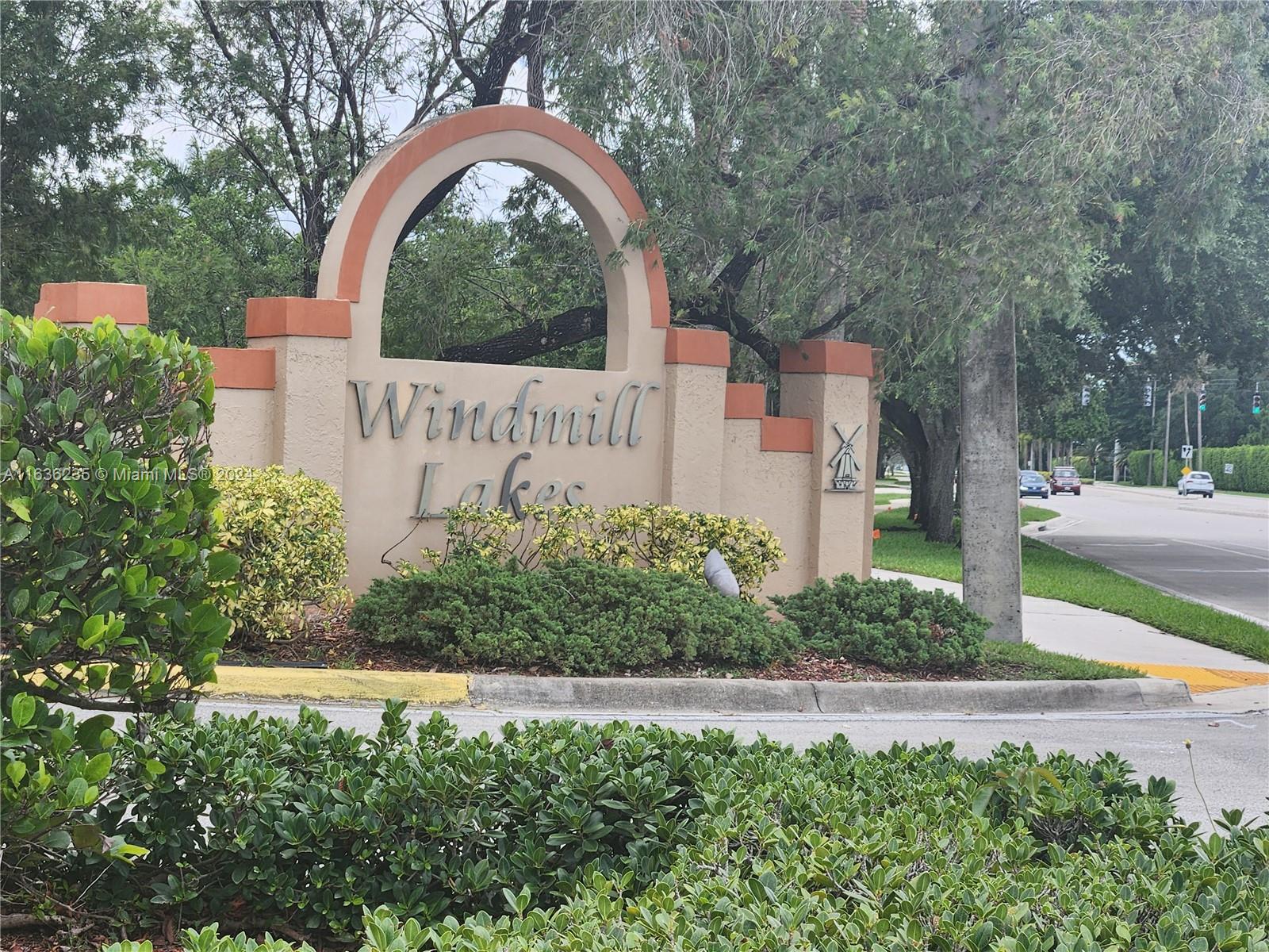 a view of sign board with yard and large trees