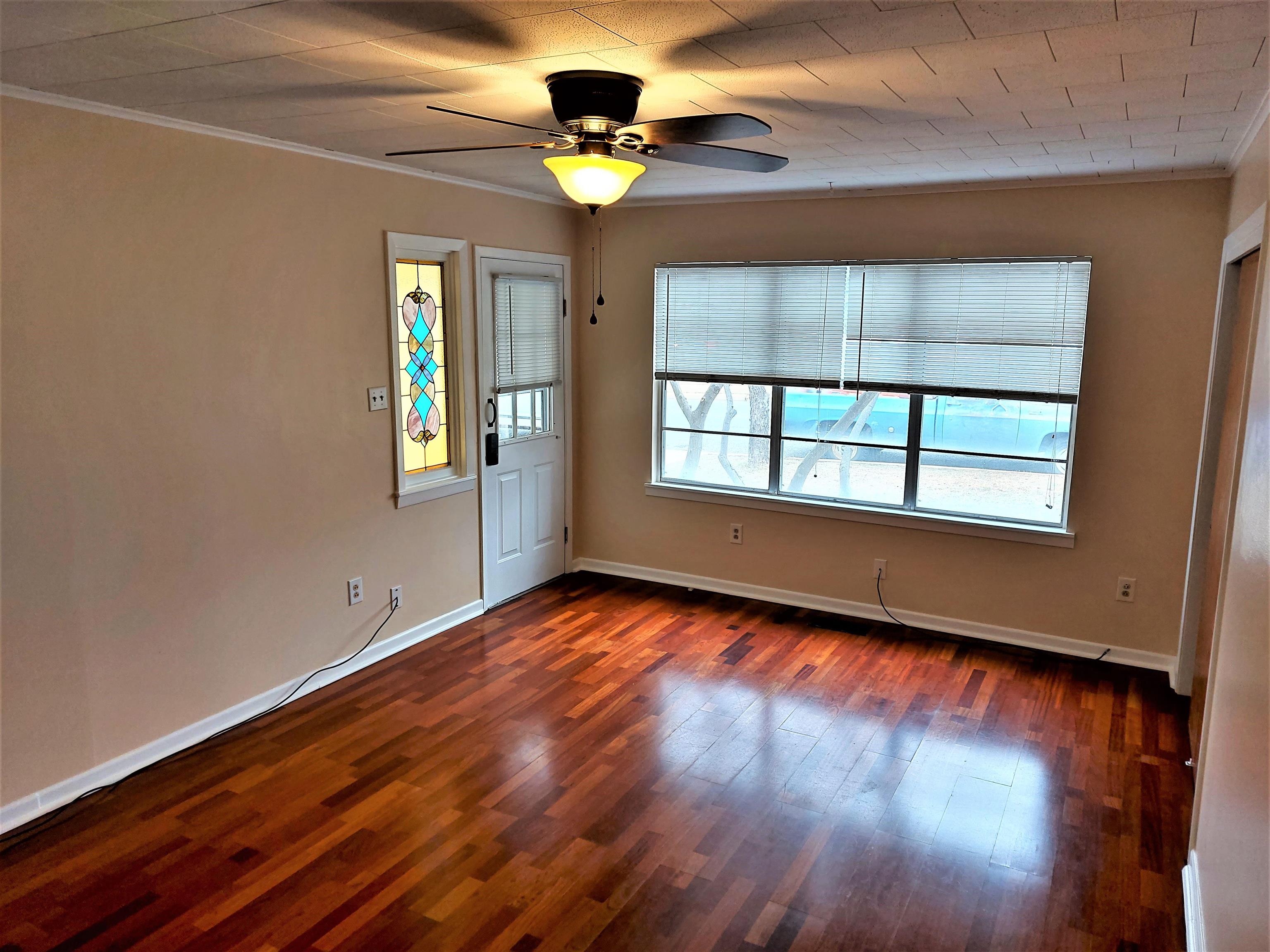 a view of an empty room with wooden floor and a window