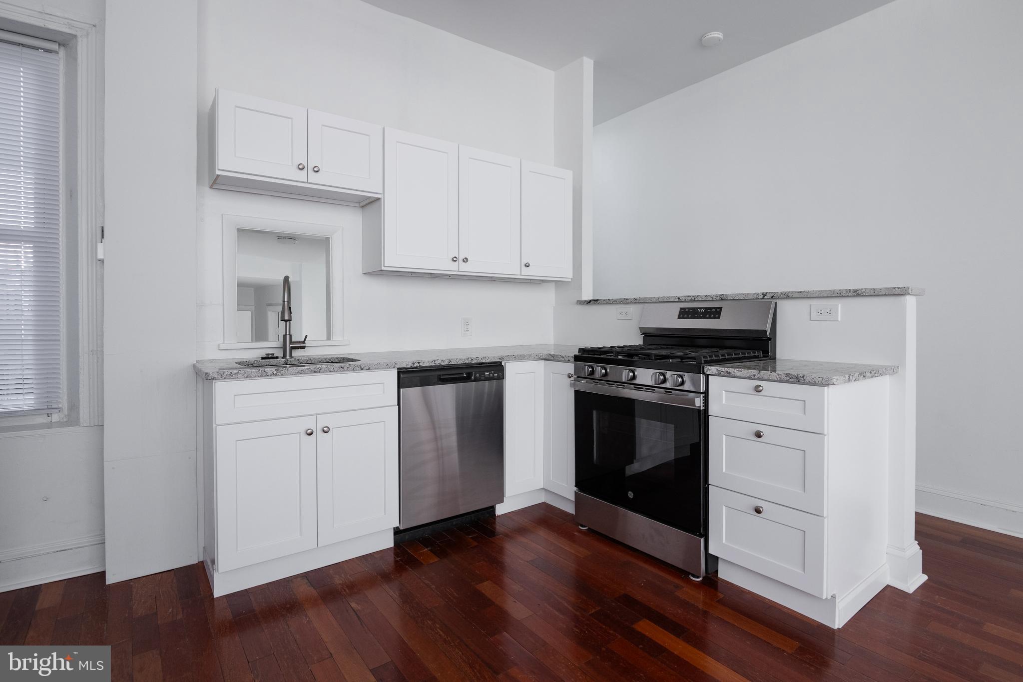 a kitchen with granite countertop white cabinets and stainless steel appliances with wooden floors