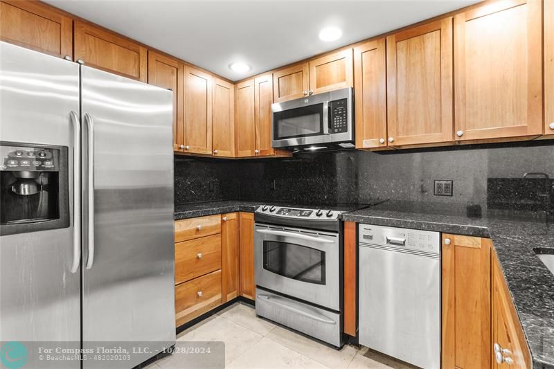 a kitchen with stainless steel appliances granite countertop a refrigerator a stove a sink and dishwasher with a white cabinets