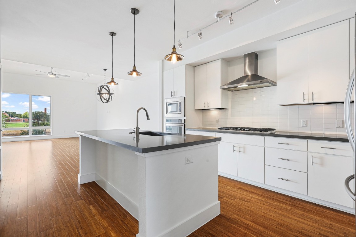 a kitchen with stainless steel appliances granite countertop a sink a stove and white cabinets with wooden floor