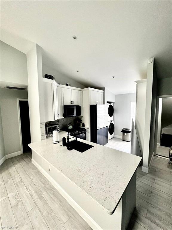 Kitchen with stacked washer and clothes dryer, black appliances, light hardwood / wood-style floors, kitchen peninsula, and white cabinetry