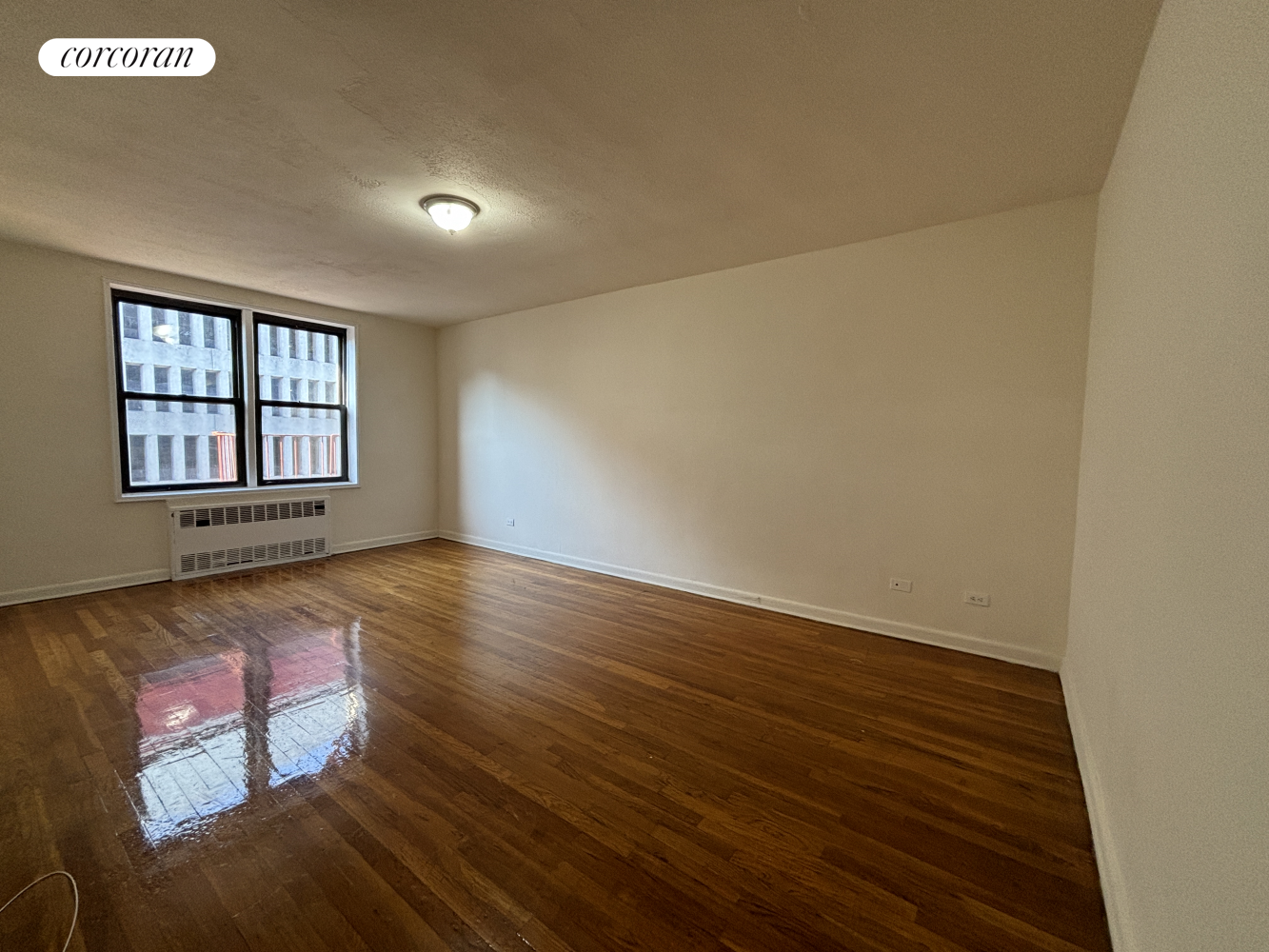 a view of an empty room with wooden floor and a window