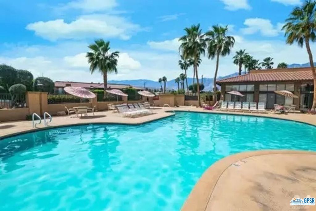 a view of a swimming pool with lawn chairs under palm trees