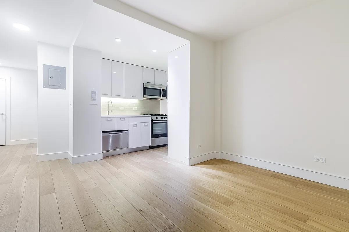 an empty room with wooden floor and entrance to kitchen