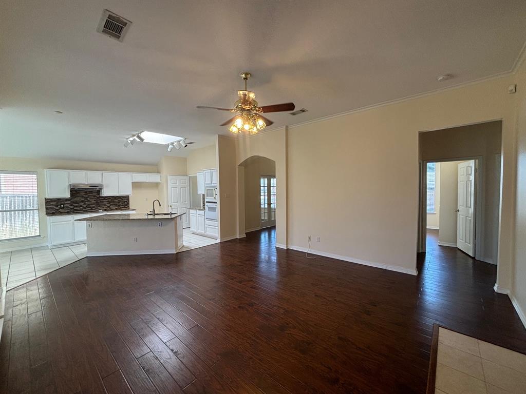 a view of an empty room with wooden floor and a kitchen