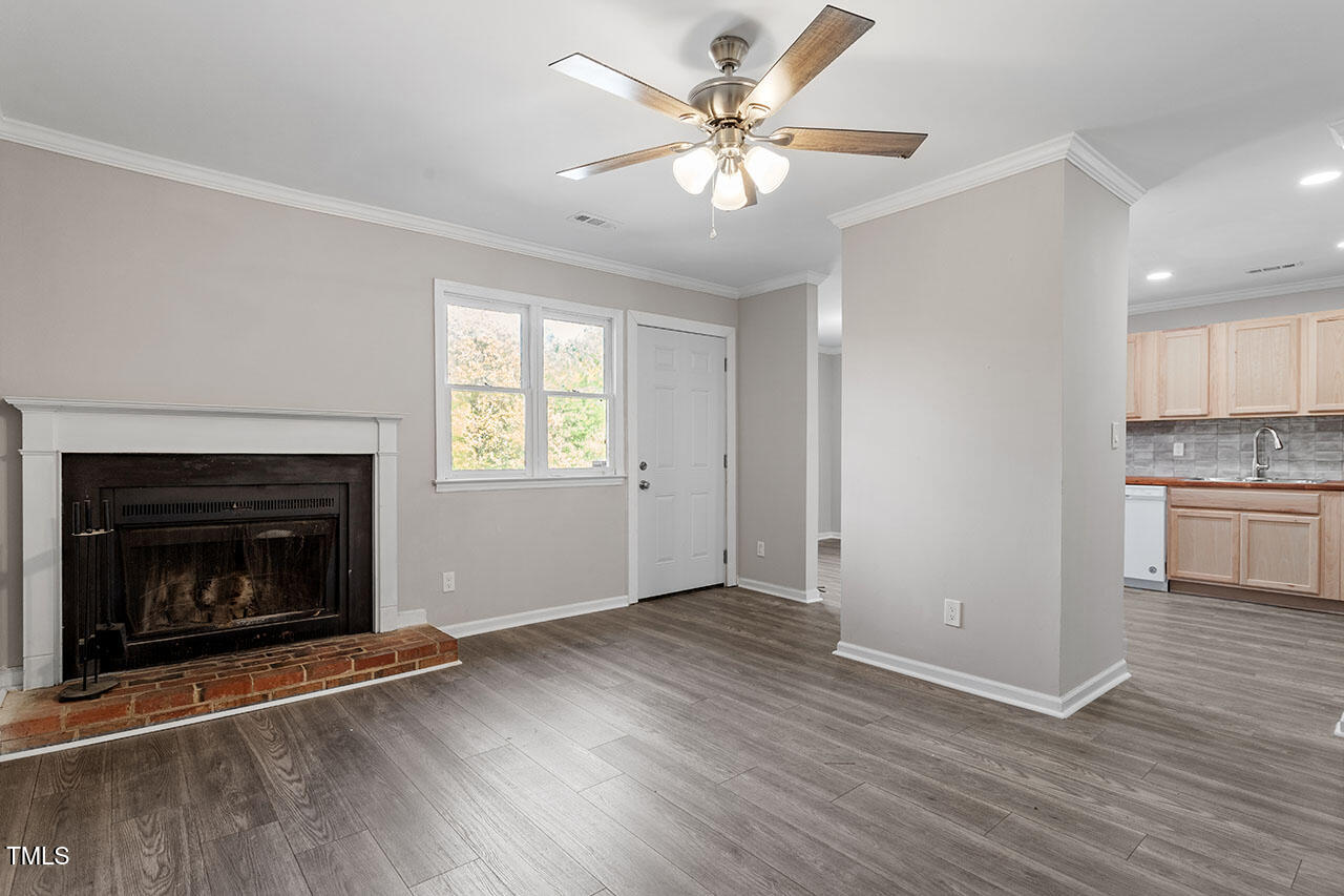 a view of an empty room with wooden floor fireplace and a window