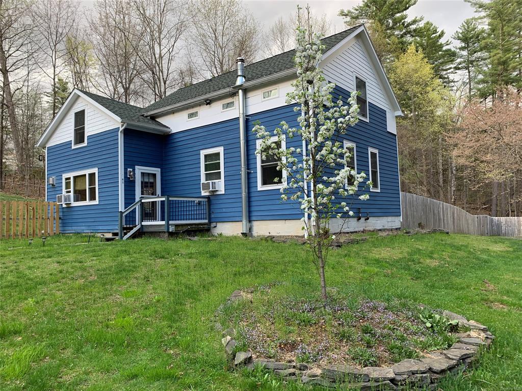 Rear view of house with a deck, cooling unit, and a lawn