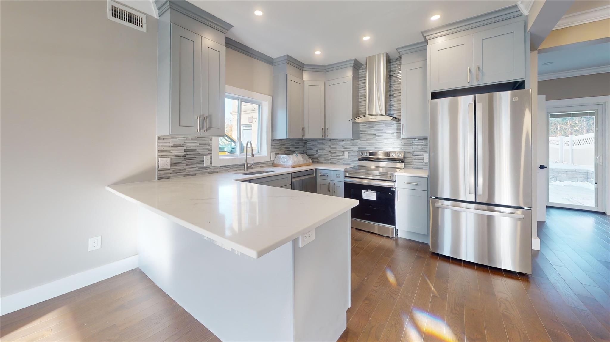 Kitchen with wall chimney range hood, crown molding, sink, gray cabinets, and appliances with stainless steel finishes