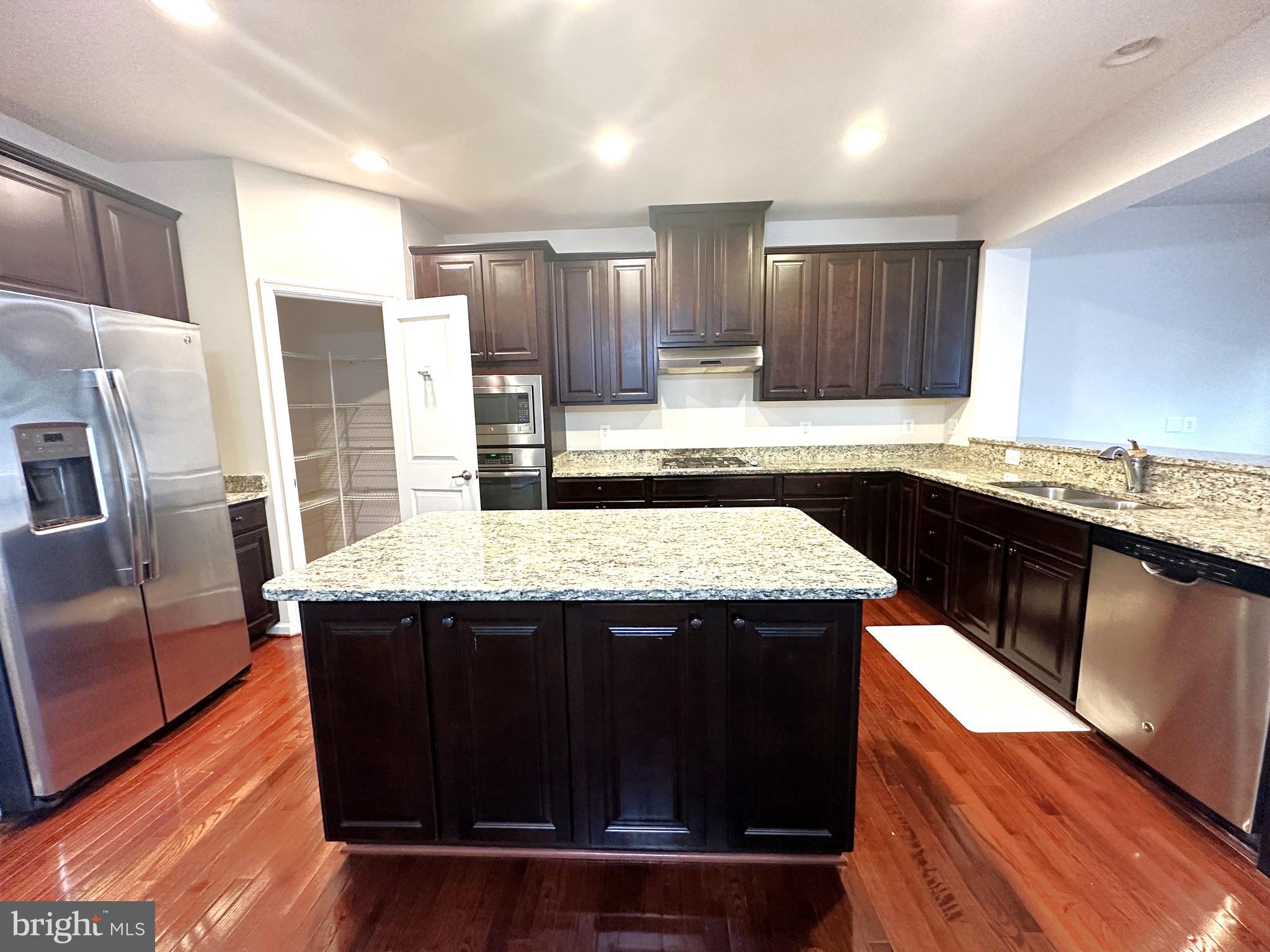 a kitchen with kitchen island stainless steel appliances a sink cabinets and wooden floor