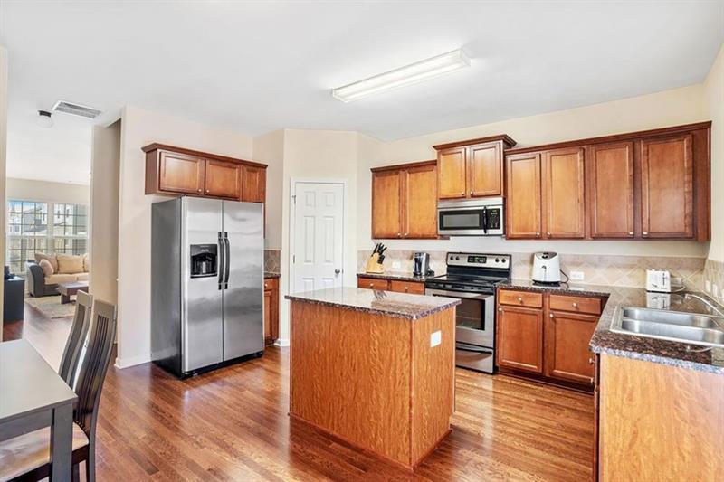 a kitchen with stainless steel appliances granite countertop a refrigerator a stove top oven a sink dishwasher and wooden cabinets with wooden floor