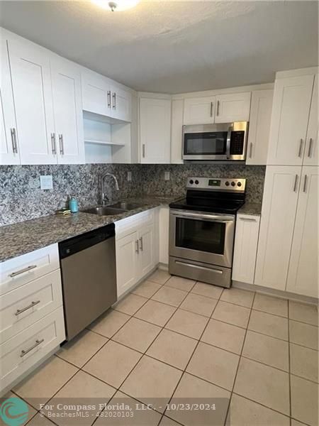 a kitchen with granite countertop a sink a stove a microwave and cabinets