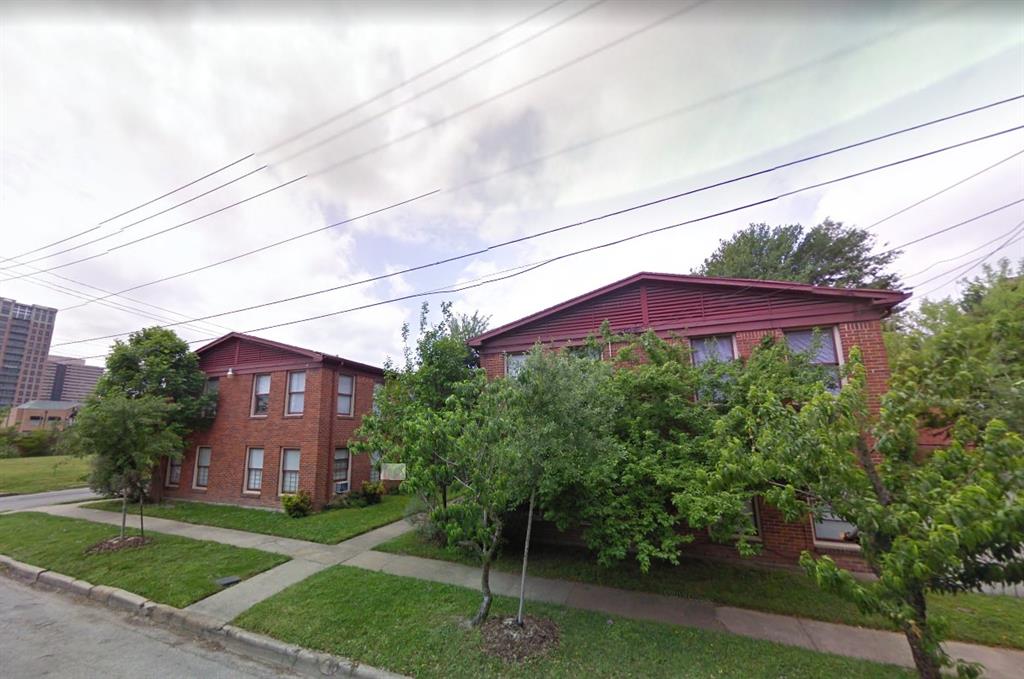 a view of a large brick house next to a yard with big trees