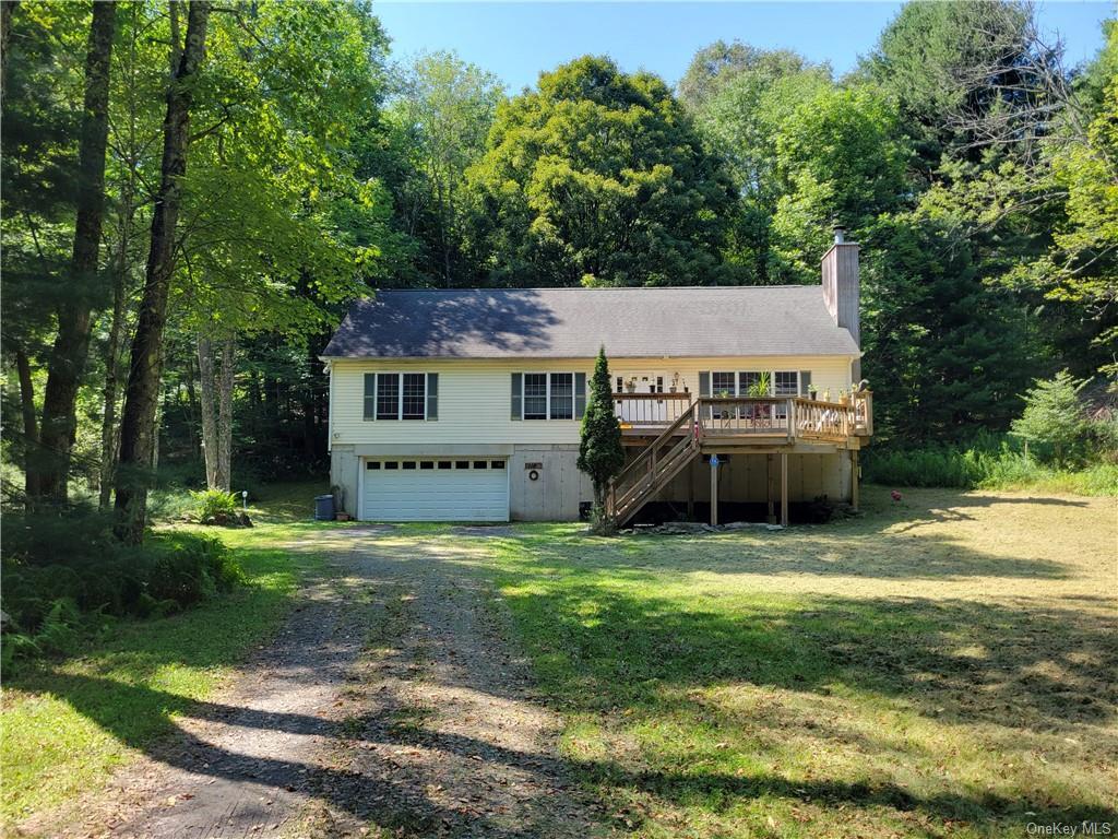 View of front facade featuring a garage, a wooden deck, and a front yard