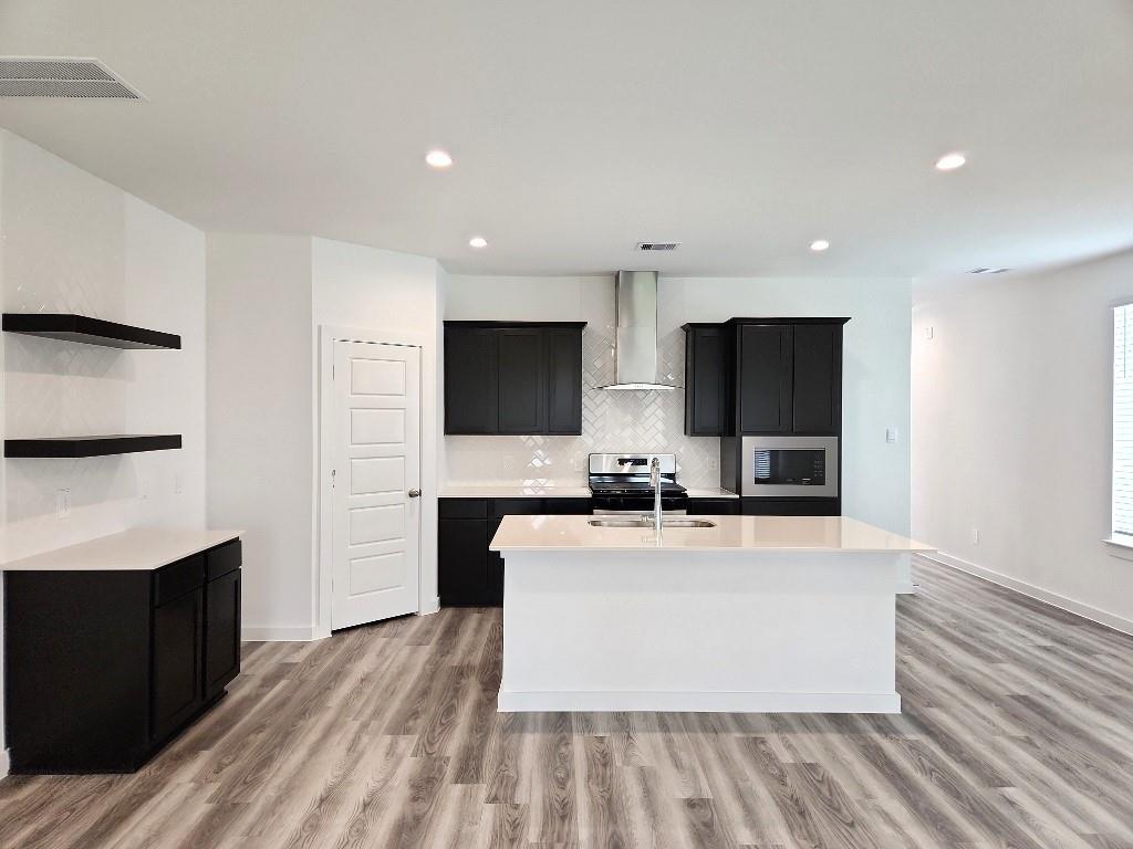 a large room with kitchen island a sink wooden floor and stainless steel appliances