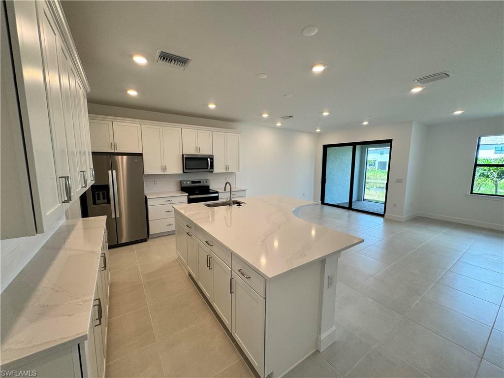 Kitchen with a center island with sink, light stone countertops, stainless steel appliances, and white cabinets