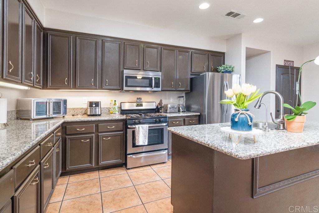 a kitchen with kitchen island granite countertop a sink dishwasher stove and refrigerator with wooden cabinets