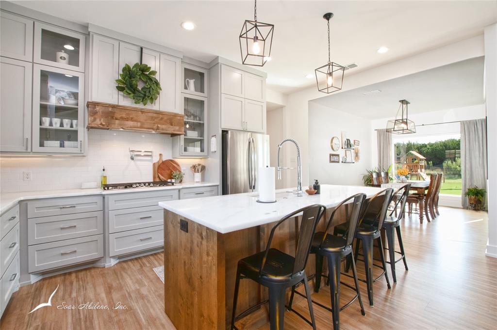 a open kitchen with stainless steel appliances granite countertop a stove a refrigerator a kitchen island a dining table and chairs with wooden floor